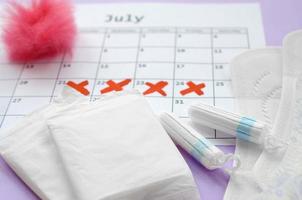 almohadillas menstruales y tampones en el calendario del período de menstruación con marcas de cruz roja sobre fondo lila foto