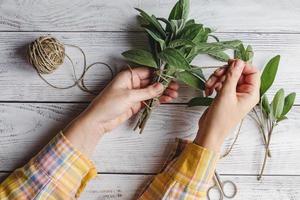 Sage leaf bundle in hands, hemp string and scissors on old wooden table photo