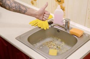 la mano de un joven tatuado se muestra como en el fondo de un fregadero de cocina sucio con una tubería obstruida foto