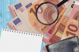 10 euro bills and magnifying glass with black purse and notepad. Concept of counterfeit money. Search for differences in details on money bills to detect fake photo