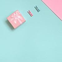 una pequeña caja de regalo rosa y dos clavijas se encuentran en el fondo de textura de papel de colores azul pastel y rosa de moda en un concepto mínimo foto