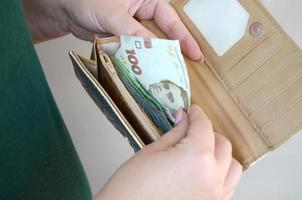 Female hands holding ukrainian hryvnia bills in small money pouch or wallet photo