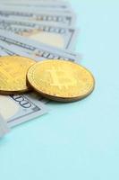 Golden bitcoins and hundred dollar bills lies on light blue background photo