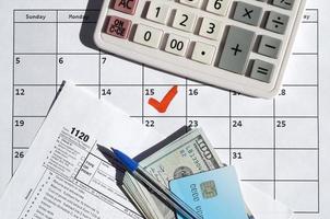 1120 Corporation Income Tax Return blank with dollar bills, calculator and pen on calendar page with marked 15th April photo