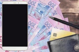 Billetes de 200 grivnas ucranianas y smartphone con monedero y tarjeta de crédito. pagos electrónicos o concepto de comercio electrónico. compras y negocios en línea con dispositivos portátiles foto
