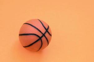 una pequeña bola naranja para el juego deportivo de baloncesto se encuentra en el fondo de textura del papel de color naranja pastel de moda en un concepto mínimo foto