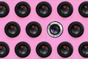 A few camera lenses with a closed aperture lie on texture background of fashion pastel pink color paper in minimal concept. Abstract trendy pattern photo