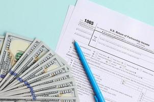 El formulario de impuestos 1065 se encuentra cerca de los billetes de cien dólares y el bolígrafo azul sobre un fondo azul claro. nosotros devolvemos los ingresos de paternidad foto