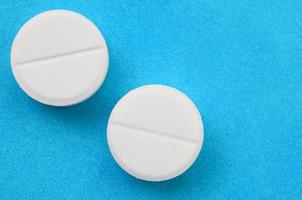 A few white tablets lie on a bright blue background surface. Background image on medical and pharmaceutical topics photo