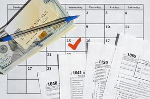 Many most important tax form blanks with credit card on dollar bills and pen on calendar page with marked 15th April photo