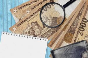 2000 Hungarian forint bills and magnifying glass with black purse and notepad. Concept of counterfeit money. Search for differences in details on money bills to detect fake photo