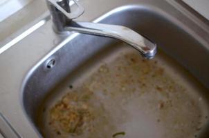 tapón del fregadero de acero inoxidable cerca del orificio lleno de agua y partículas de comida foto