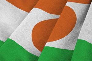 Niger flag with big folds waving close up under the studio light indoors. The official symbols and colors in banner photo