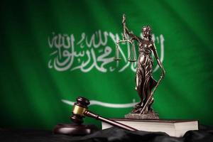 bandera de arabia saudita con estatua de la dama de la justicia, constitución y martillo de juez sobre cortinas negras. concepto de juicio y culpa foto
