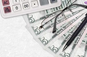 Ventilador de billetes de 5 dólares estadounidenses y calculadora con gafas y bolígrafo. préstamo comercial o concepto de temporada de pago de impuestos foto