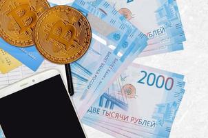 Billetes de 2000 rublos rusos y bitcoins dorados con smartphone y tarjetas de crédito. concepto de inversión en criptomonedas. criptominería o comercio foto