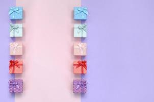 Small gift boxes of different colors with ribbons lies on a violet and pink color background photo