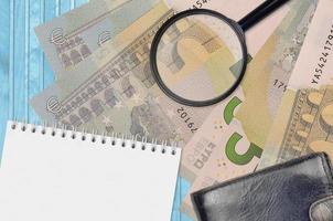 5 euro bills and magnifying glass with black purse and notepad. Concept of counterfeit money. Search for differences in details on money bills to detect fake photo