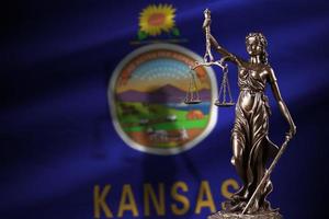 bandera del estado de kansas us con estatua de la dama de la justicia y escalas judiciales en una habitación oscura. concepto de juicio y castigo foto