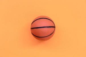 una pequeña bola naranja para el juego deportivo de baloncesto se encuentra en el fondo de textura del papel de color naranja pastel de moda en un concepto mínimo foto