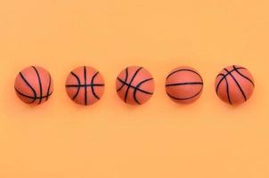 muchas pelotas naranjas pequeñas para el juego deportivo de baloncesto se encuentran en el fondo de textura del papel de color naranja pastel de moda en un concepto mínimo foto