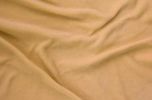 The blanket of furry orange fleece fabric. A background of light orange soft plush fleece material with a lot of relief folds photo