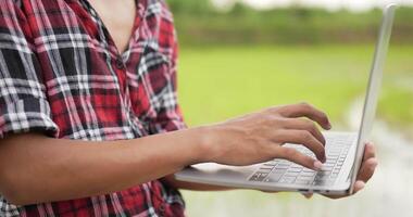 Close up shot Hand of young farmer typing laptop keyboard at rice field. He taping and typing data on laptop computer video