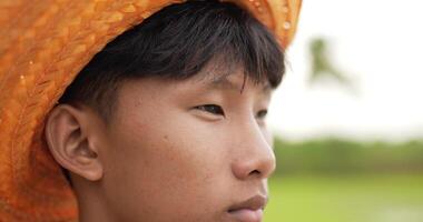 Slow motion Head shot, Portrait of young farmer wearing plaid shirt and straw hat wiping sweat on forehead with tired and hot weather at rice field video