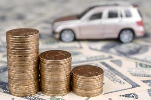 Toy car model at the stacks of golden coins lies on many dollar bills photo