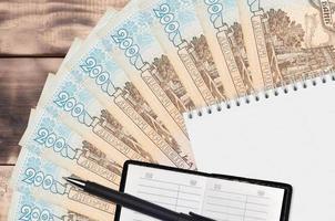 Ventilador de billetes de 200 hryvnias ucranianas y bloc de notas con libreta de contactos y bolígrafo negro. concepto de planificación financiera y estrategia empresarial foto