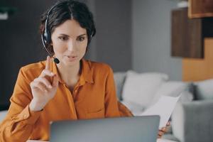 joven tutora española con auriculares mirando la pantalla de un portátil durante la clase en línea