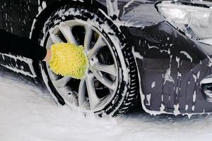 Workers hand with yellow sponge washing car wheels with detergent for cleaning vehicles. Maintenance and service concept photo