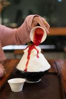 postre de hielo raspado coreano con coberturas dulces, bingsu de fresa en mesa de madera foto