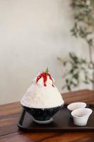 postre de hielo raspado coreano con coberturas dulces, bingsu de fresa en mesa de madera foto