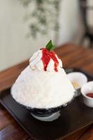 postre de hielo raspado coreano con coberturas dulces, bingsu de fresa en mesa de madera foto