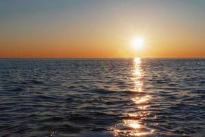 una puesta de sol soleada en el mar que se extiende hacia el horizonte con un camino y reflejos en el mar. foto