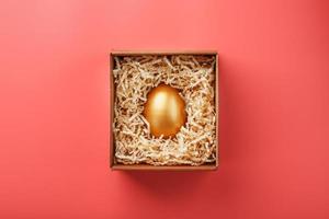 Golden egg in a box on a pink background. The concept of exclusivity, best choice, prize, special surprise, expensive gift. photo