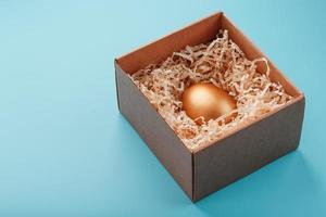 Egg made of gold in a wooden box on a blue background. The concept of exclusivity and superprize. Minimalistic composition. photo