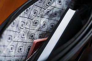 Black notebook peeking out of the pocket of a black leather bag close-up, macro Handmade, natural materials. photo