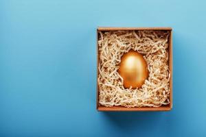 Golden egg in a box on a blue background Concept of exclusivity, best choice, prize, special surprise, expensive gift. photo