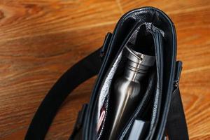 A black notebook and a bottle are in the pocket of a black leather bag close-up, macro handmade, natural materials. photo