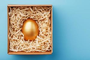 Golden egg in a box on a blue background Concept of exclusivity, best choice, prize, special surprise, expensive gift. photo