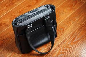 Black notebook peeking out of the pocket of a black leather bag close-up, macro Handmade, natural materials. photo