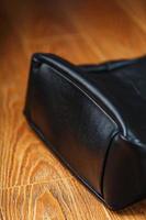 Black notebook peeking out of the pocket of a black leather bag close-up, macro Handmade, natural materials. photo