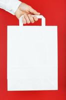 Paper bag at arm's length, white craft bag for takeaway isolated on red background. Packaging template layout with space for copying, advertising. photo