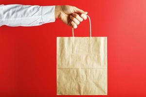 Paper bag at arm's length, brown craft bag for takeaway isolated on red background. Packaging template layout with space for copying, advertising. The concept of service delivery. photo