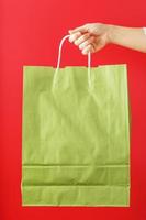 Green paper bag at arm's length isolated on a red background. Layout of the packaging template with space for copying, advertising. photo