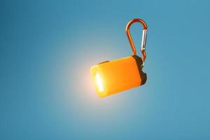 Orange led Flashlight with a carabiner on a blue background. LED lights in flight. photo