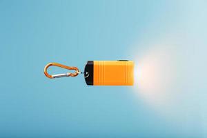 Orange led Flashlight with a carabiner on a blue background. LED lights in flight. photo