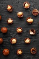 Purified and shell repeats macadamia nuts on black textural stone background. Healthy eating concept photo